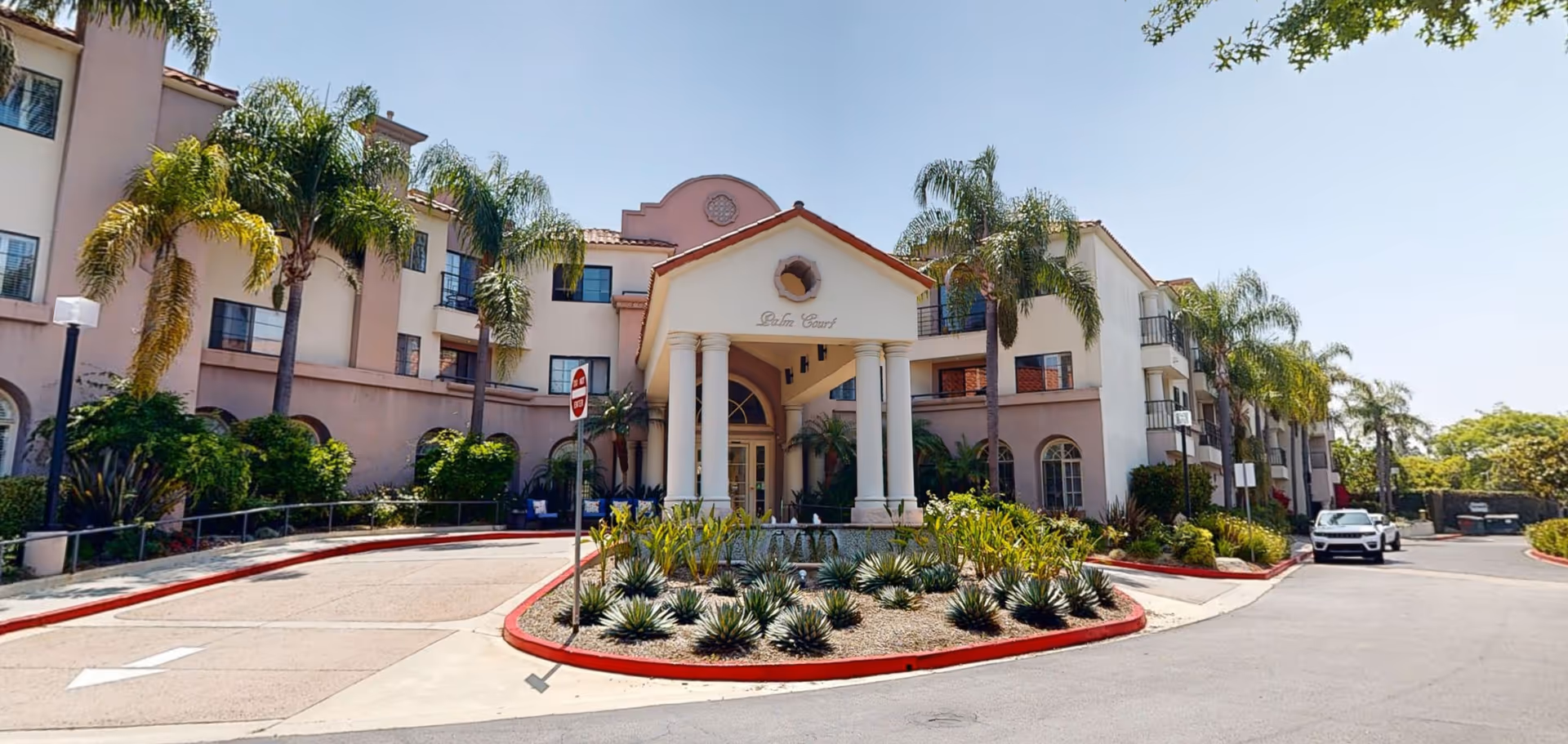 Exterior view of Palm Court senior living facility with palm trees and a circular driveway.