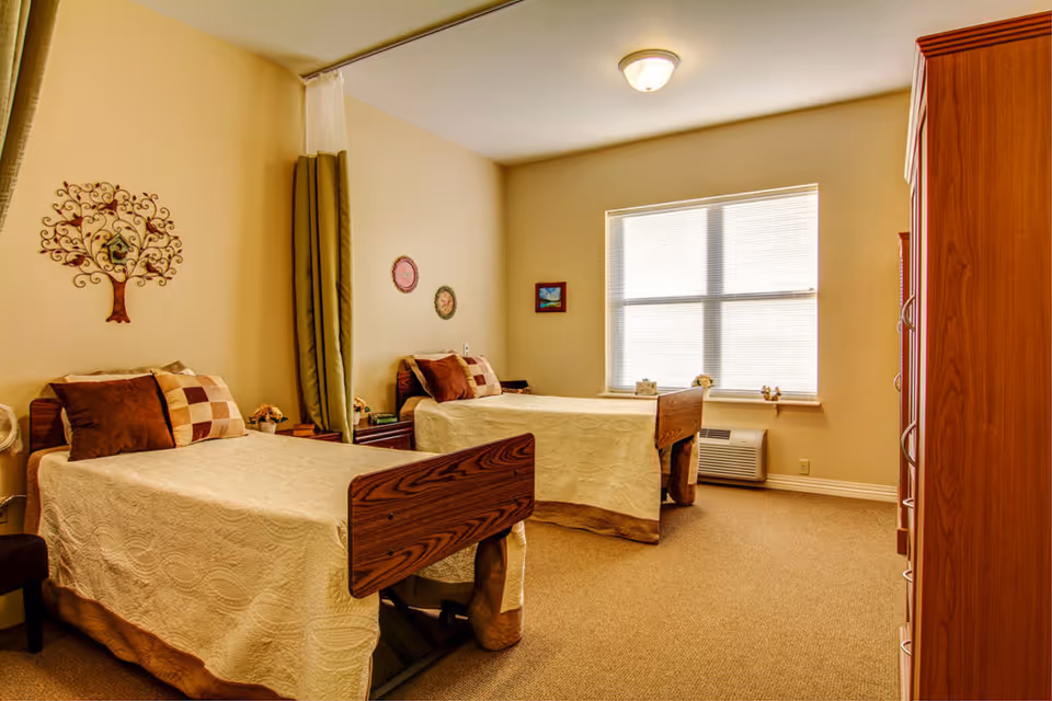 Bright bedroom with two twin beds, quilted bedspreads, decorative pillows, a large window and wooden furniture.
