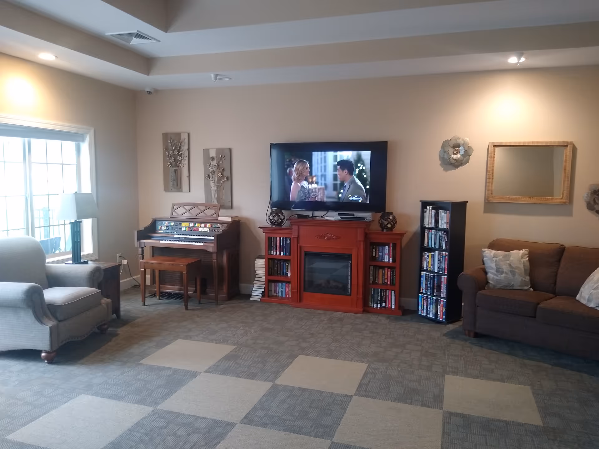 Cozy living room in a senior facility with TV, couch, armchair, and piano.