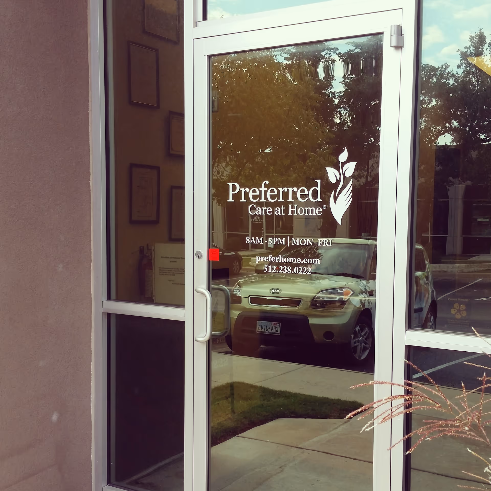 Glass entry door shows Preferred Care at Home logo; car and trees reflected outside.