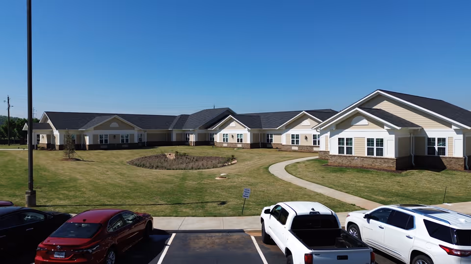 Single-story health and rehabilitation campus buildings arranged around a grassy courtyard with a curved walkway and parked cars in front.