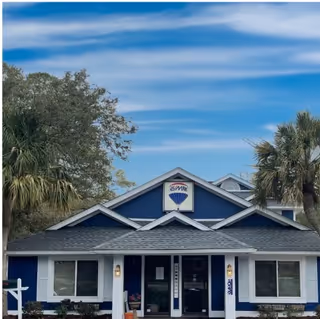 Blue clubhouse-style senior living facility with palm trees and a clear sky.