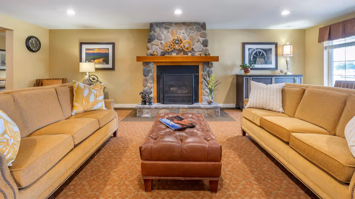 Cozy living room with two tan sofas facing a tufted leather ottoman and a stone fireplace.