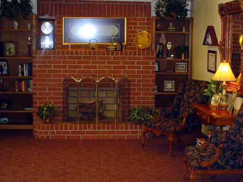 Cozy indoor common area featuring a brick fireplace, bookshelves, and upholstered seating.