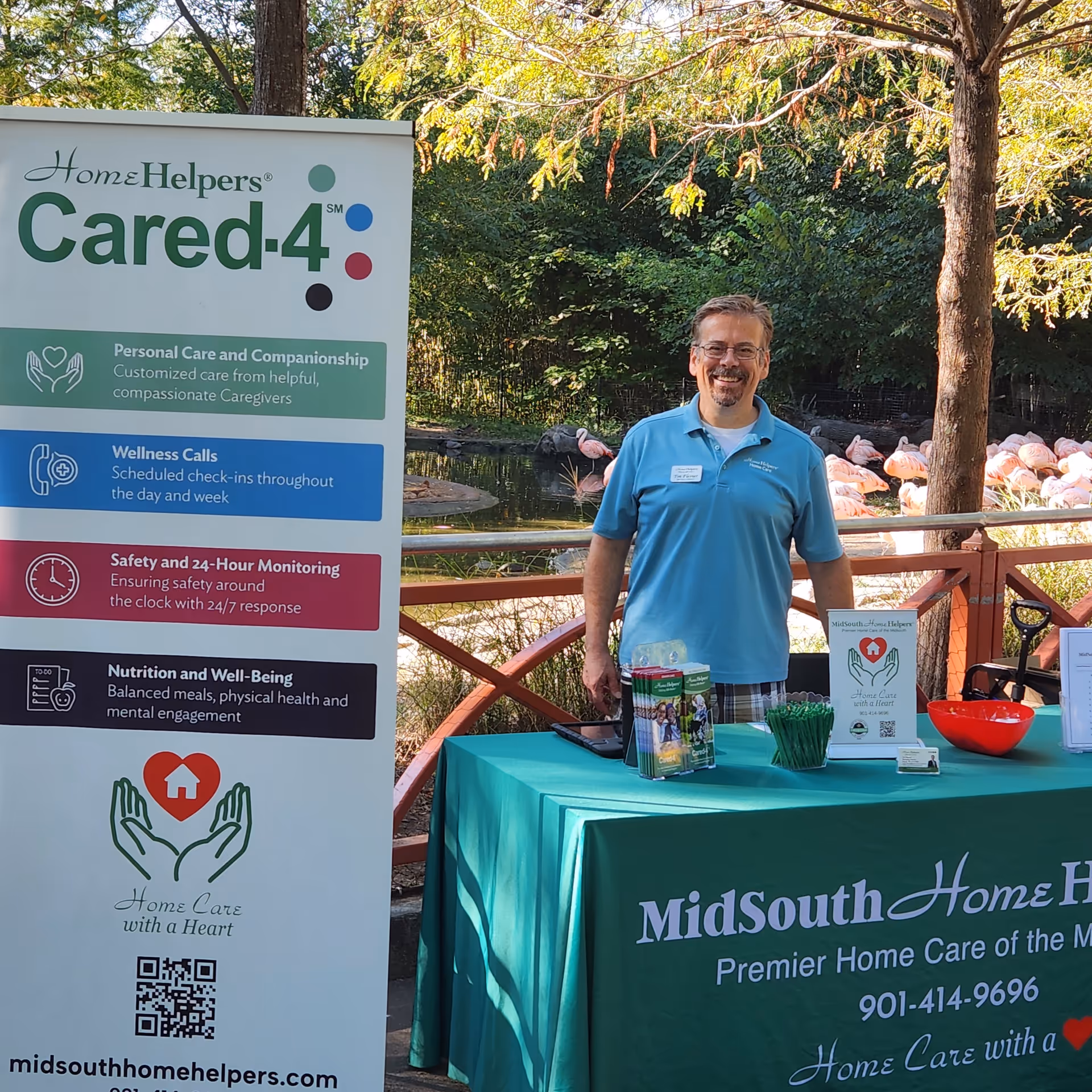A man in a blue polo stands beside a promotional banner at an outdoor care event.