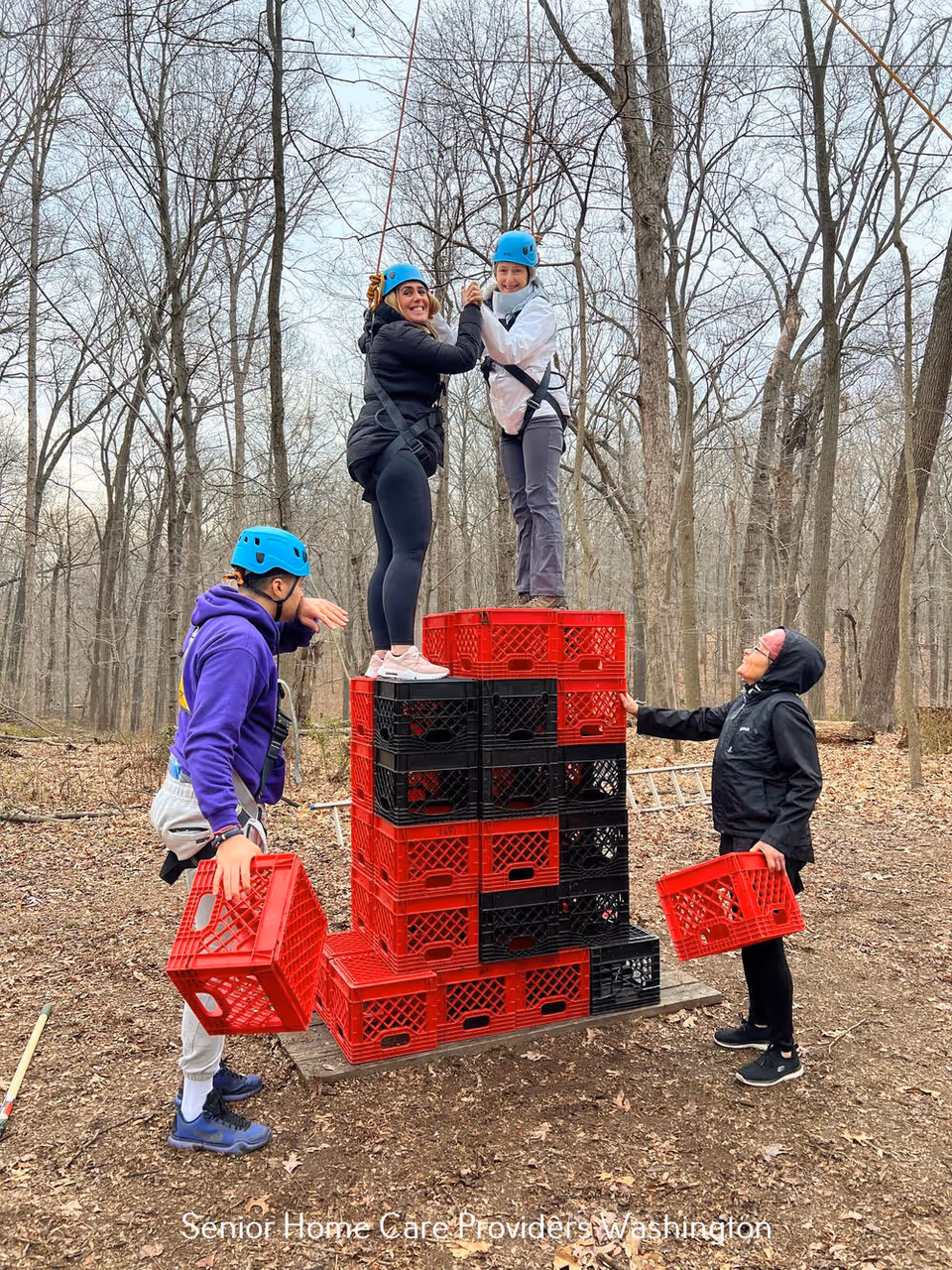 People wearing helmets stack crates outdoors in a forest.