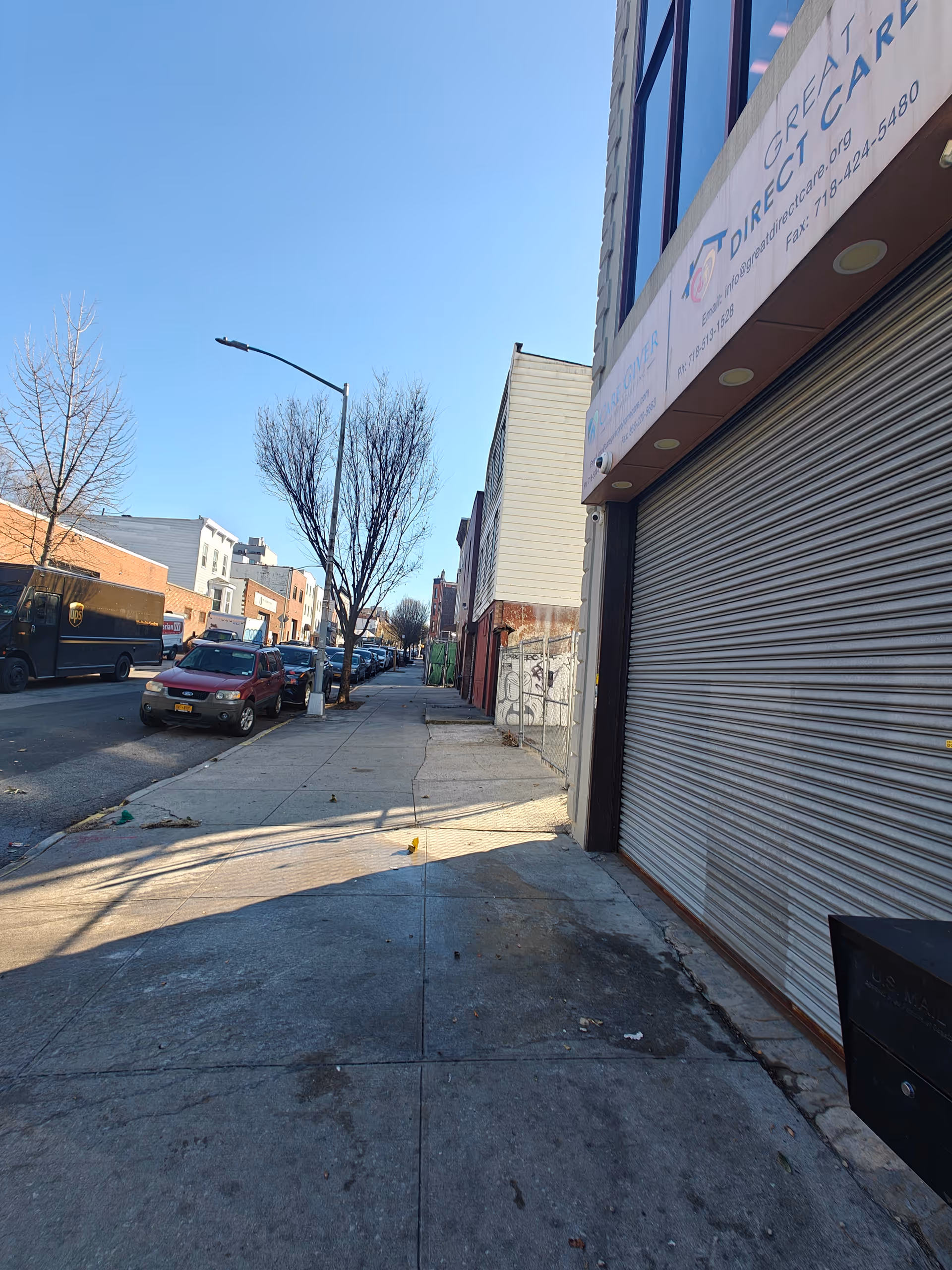 Urban street view of storefront with closed shutter, Tradition Choice sign, parked cars, bare trees.