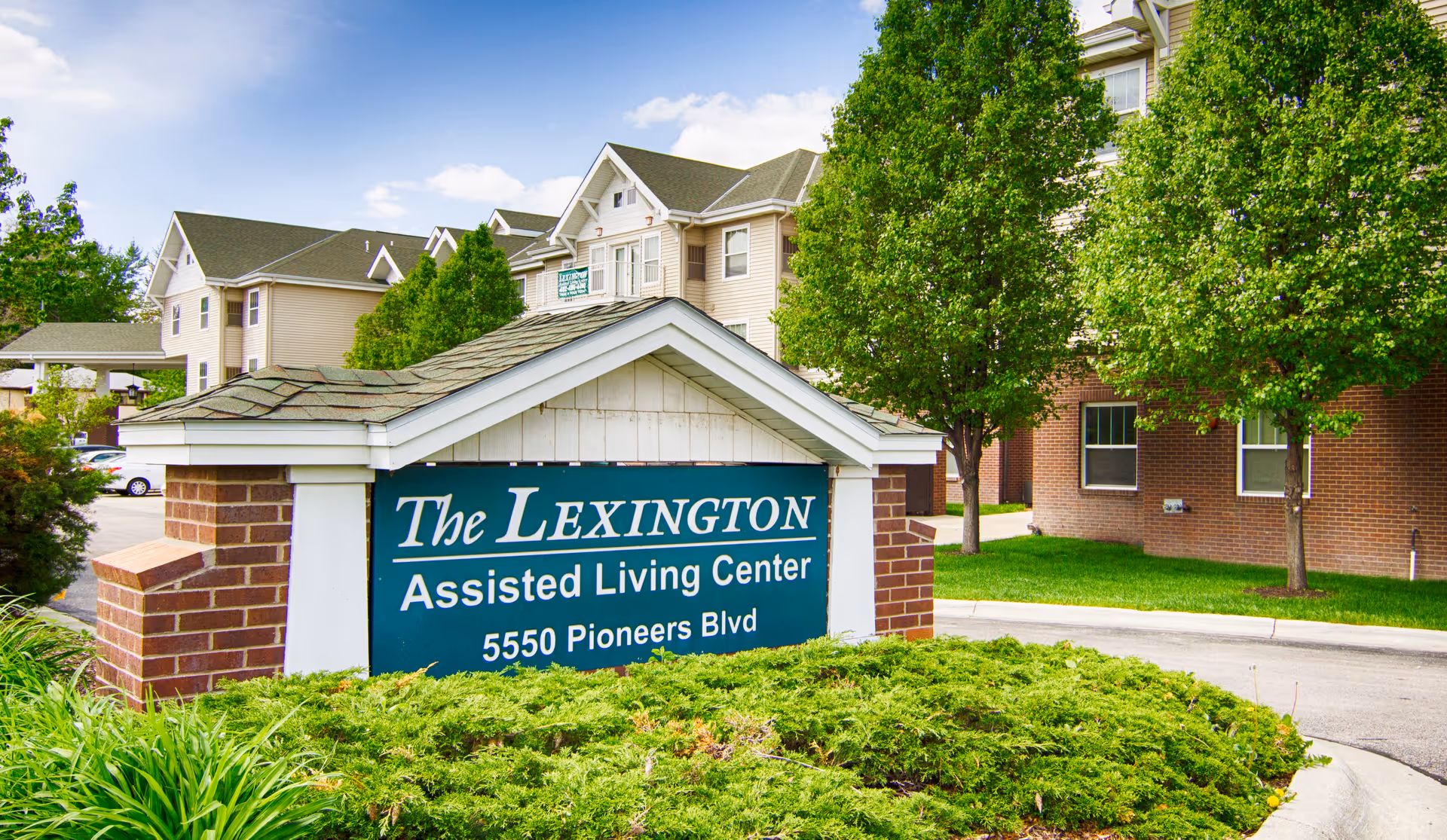 Exterior view of The Lexington Assisted Living Center sign with brick building and trees.