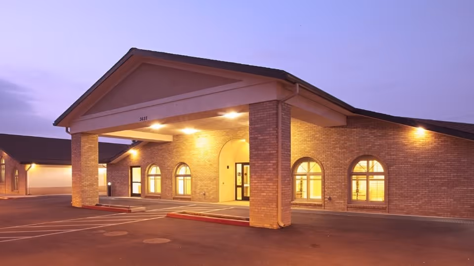 Exterior view of Arlington Gardens Care Center with illuminated entrance under a covered porte-cochère.