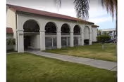White building with arched entryway and a grassy lawn on a sunny campus.