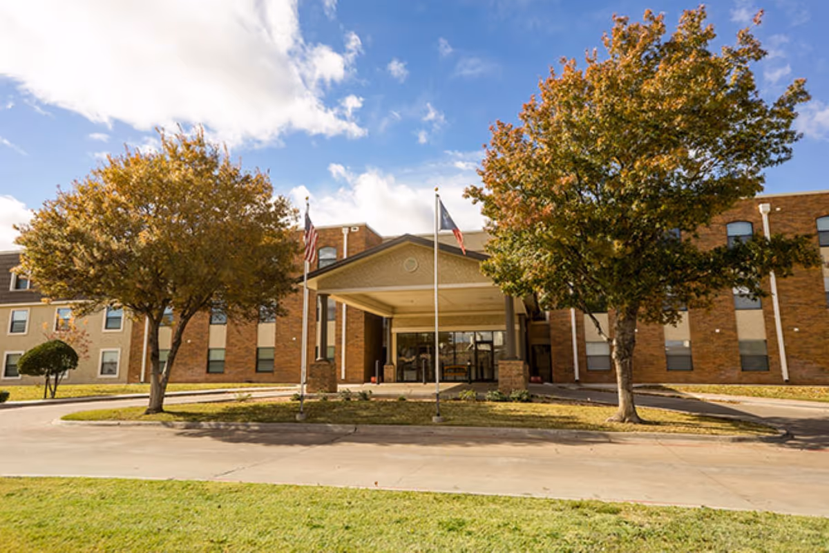 Brookdale Grand Court Lubbock exterior with entrance canopy, flags, and autumn trees.