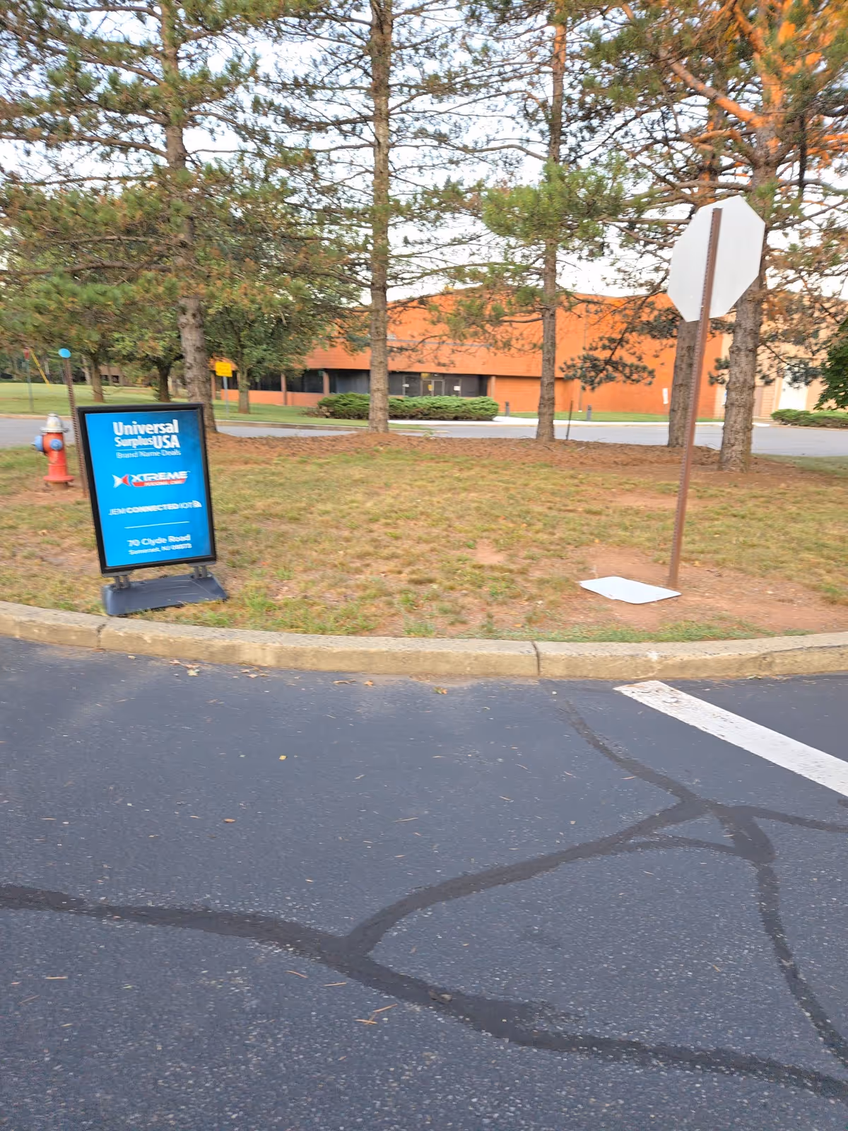 Exterior view of a facility with a blue sign, trees, and brick building.