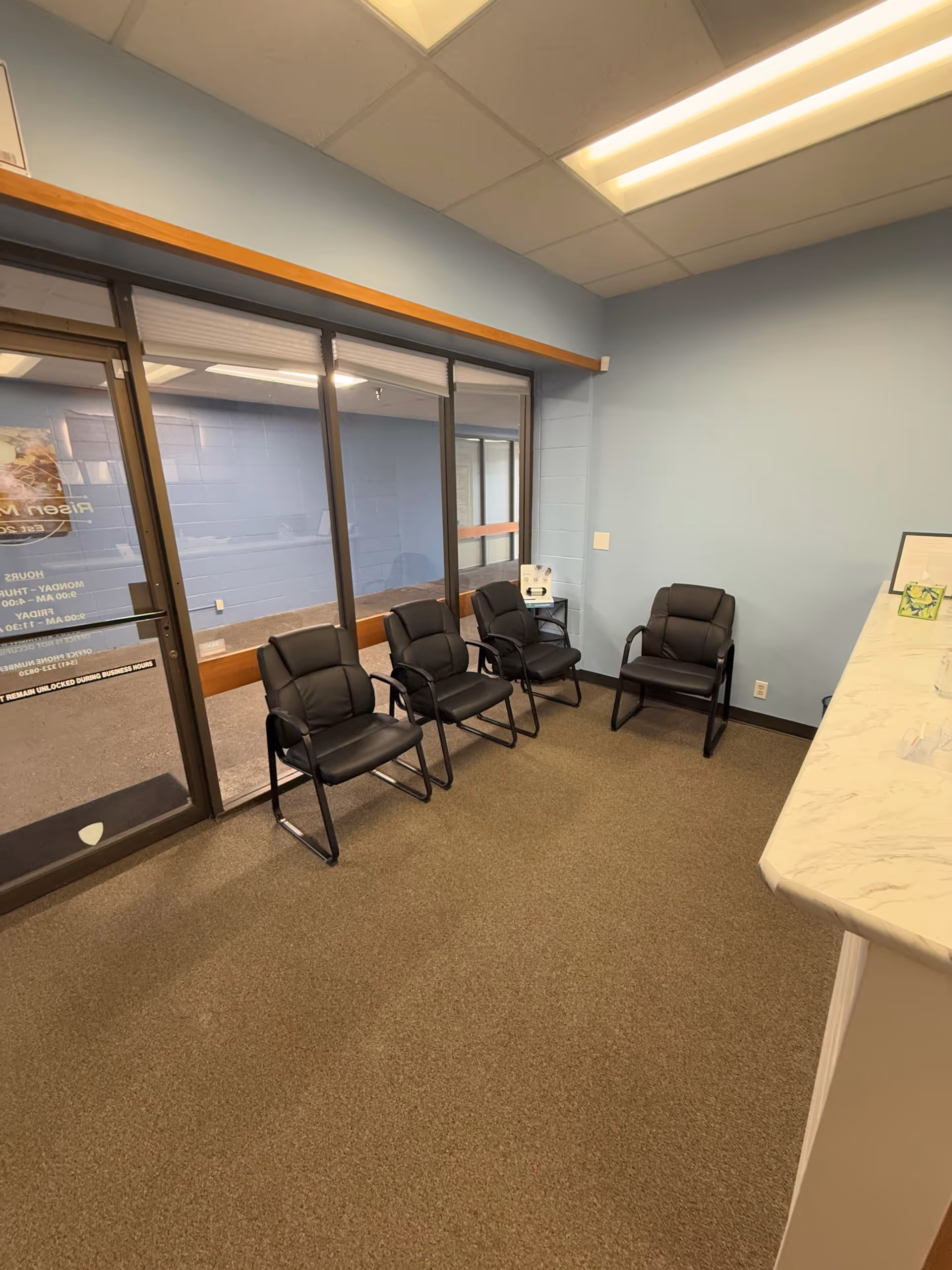 Interior waiting area with five black chairs, glass doors, and a marble counter.