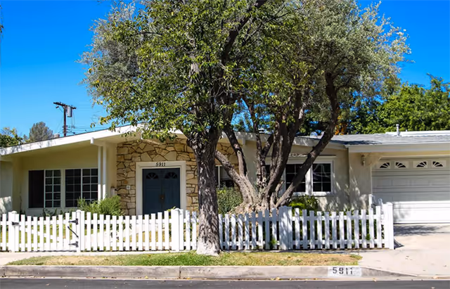 Facade of a single-story senior living facility with a white picket fence and tree