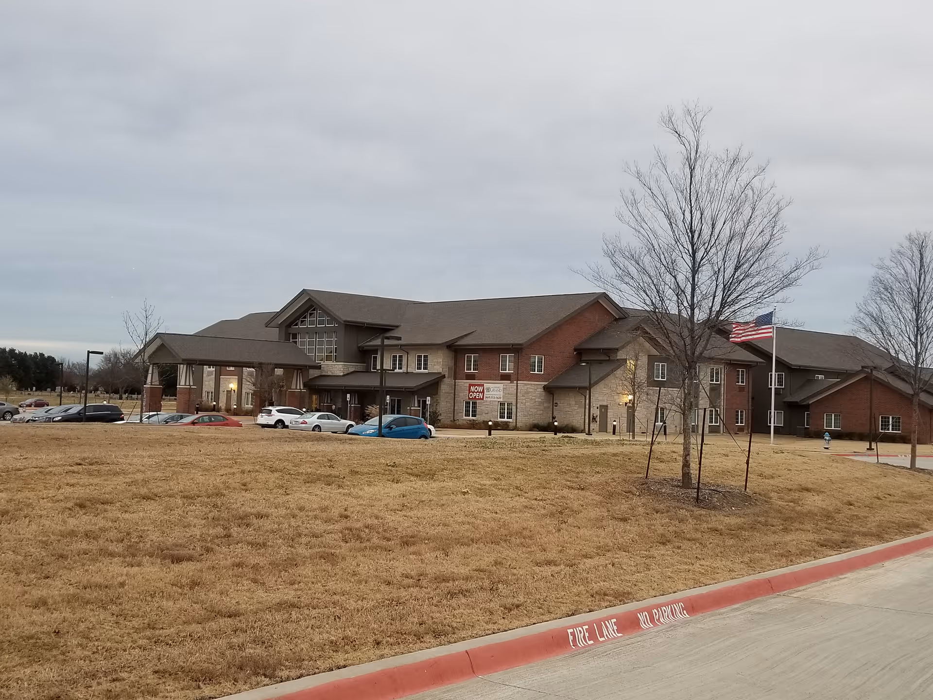 Exterior view of The Oxford Grand Assisted Living & Memory Care building with parking and flag.