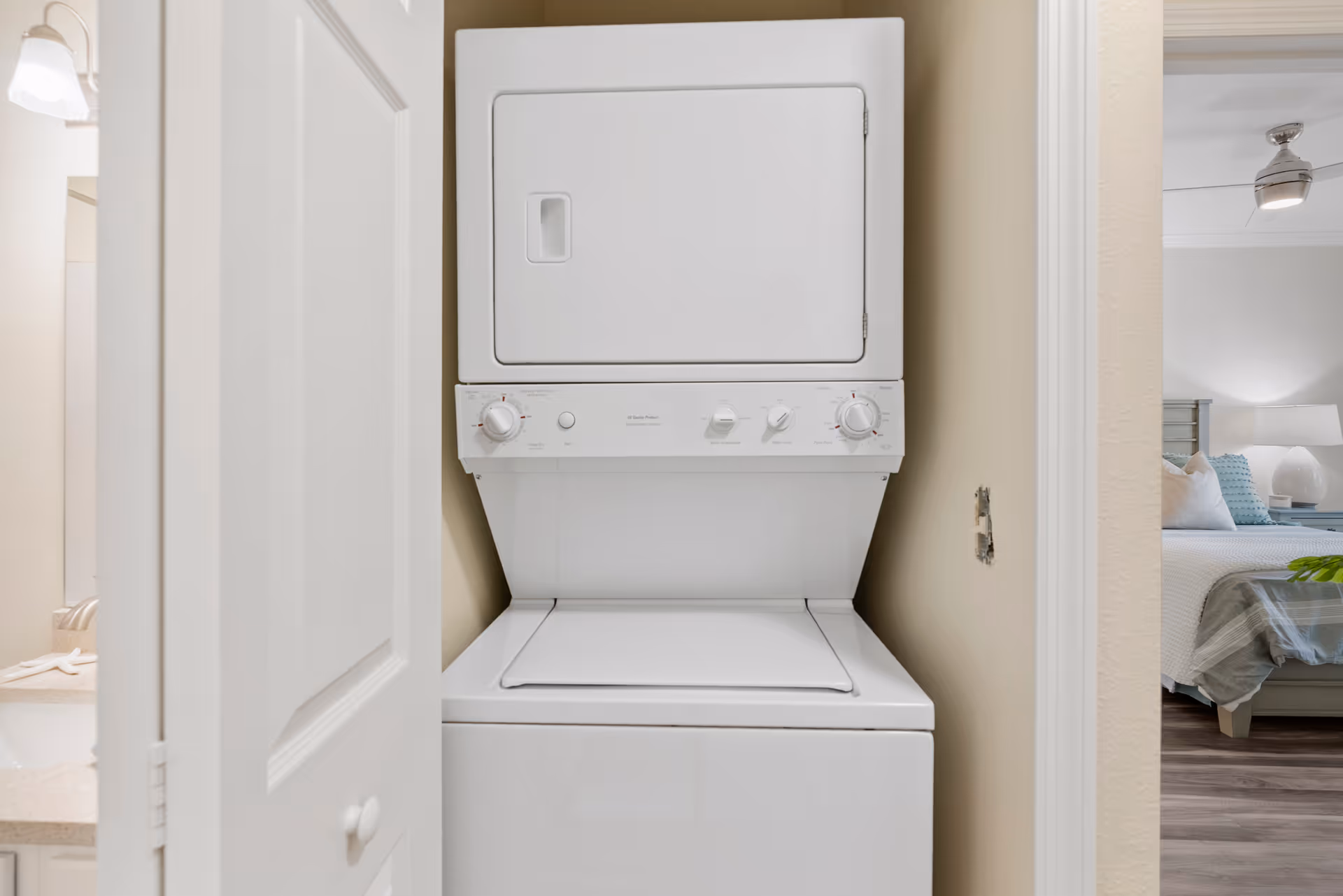 Stacked washer and dryer in a narrow laundry alcove beside a bedroom.