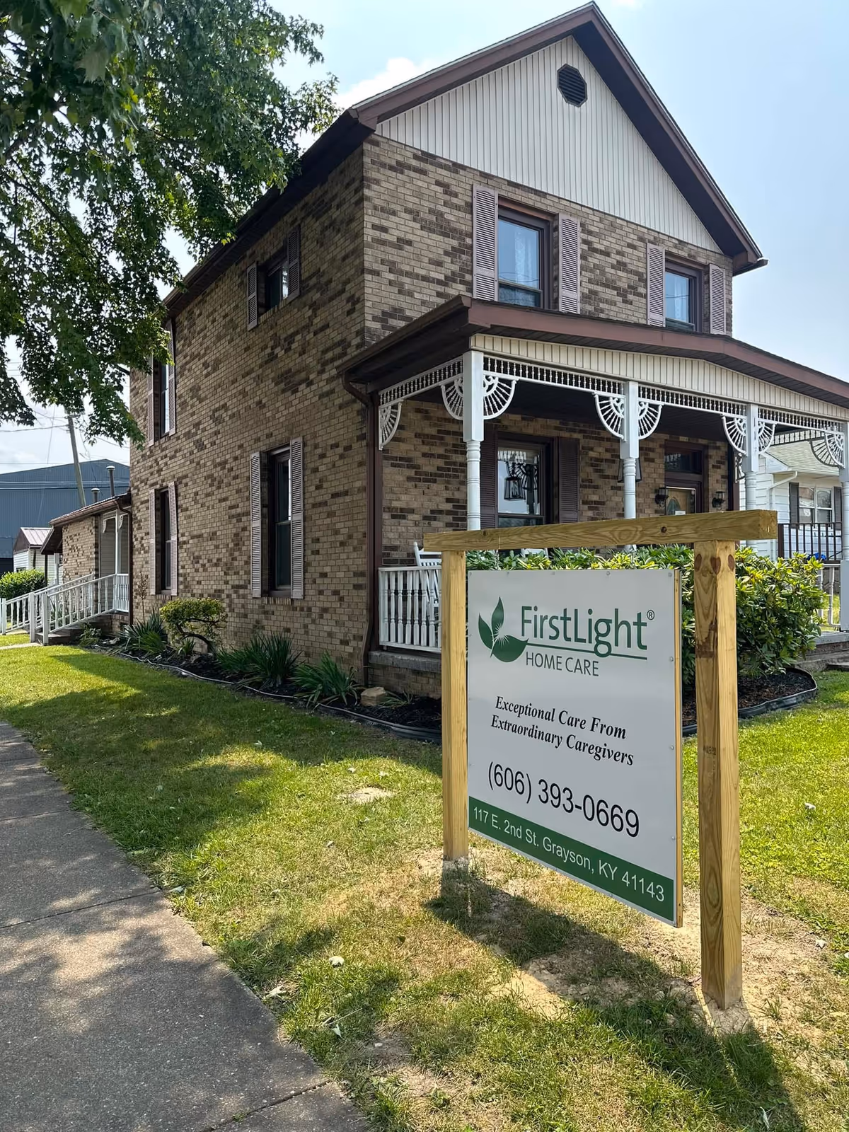 Two-story brick building with a shaded front porch and a FirstLight Home Care sign.