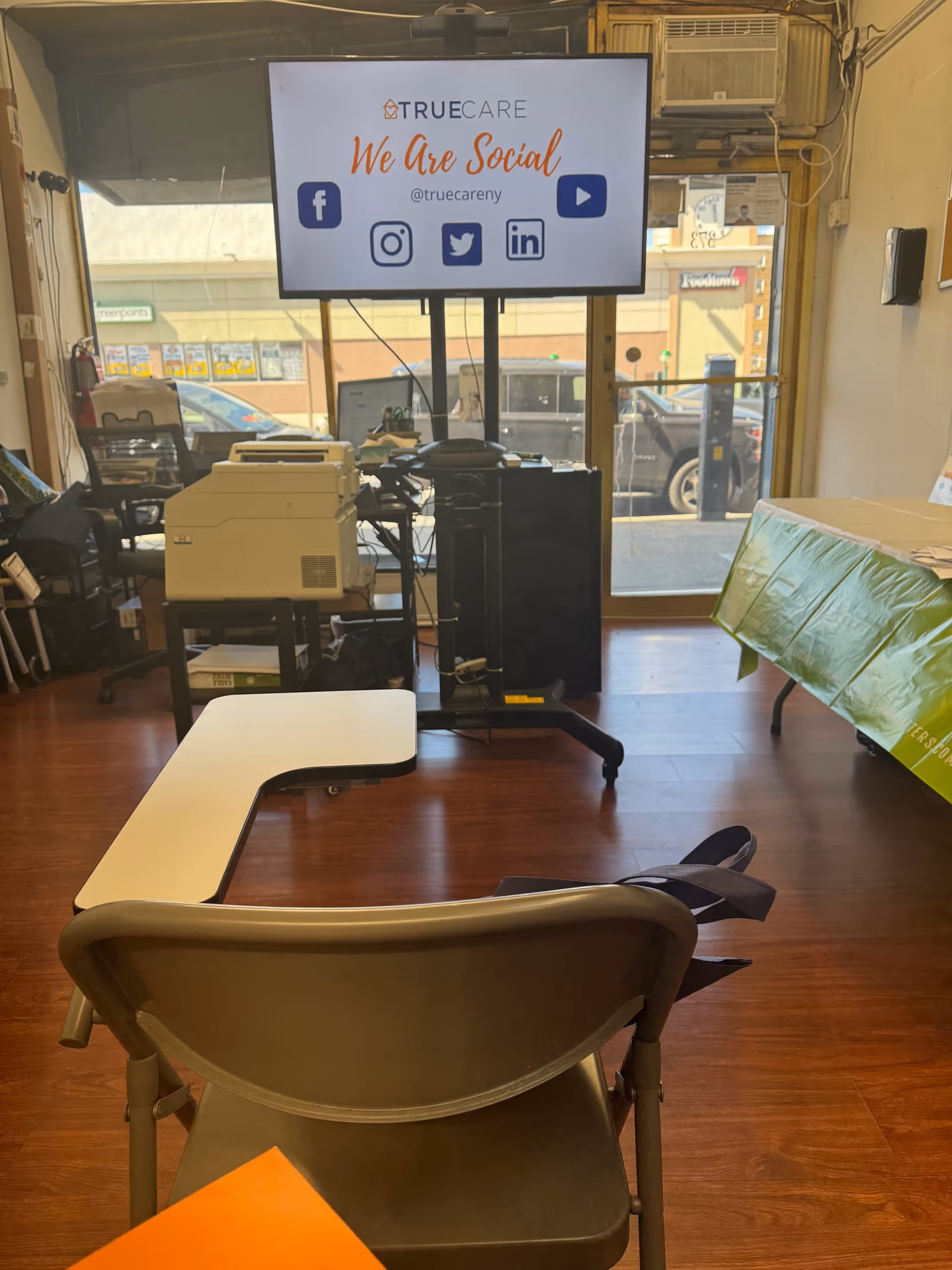 Interior office space with a large screen, printers, and a curved desk in front of windows.
