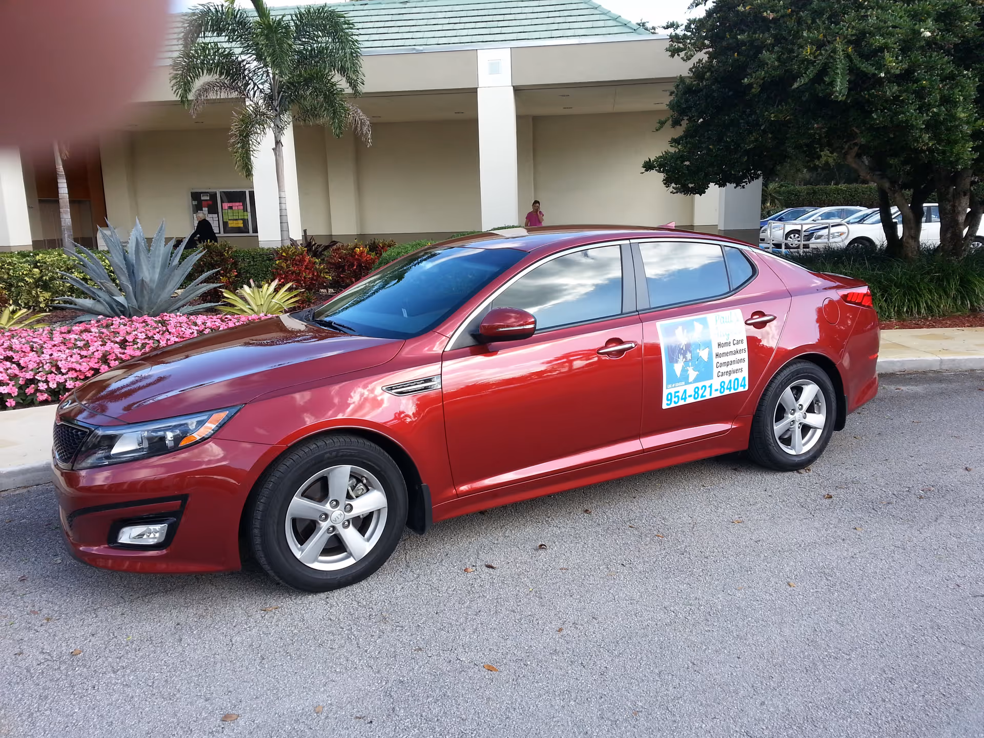 Red sedan with home care signage parked outside a senior care facility