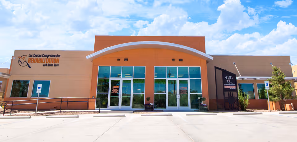 Front exterior of a beige and orange facility with glass entrance and parking area.