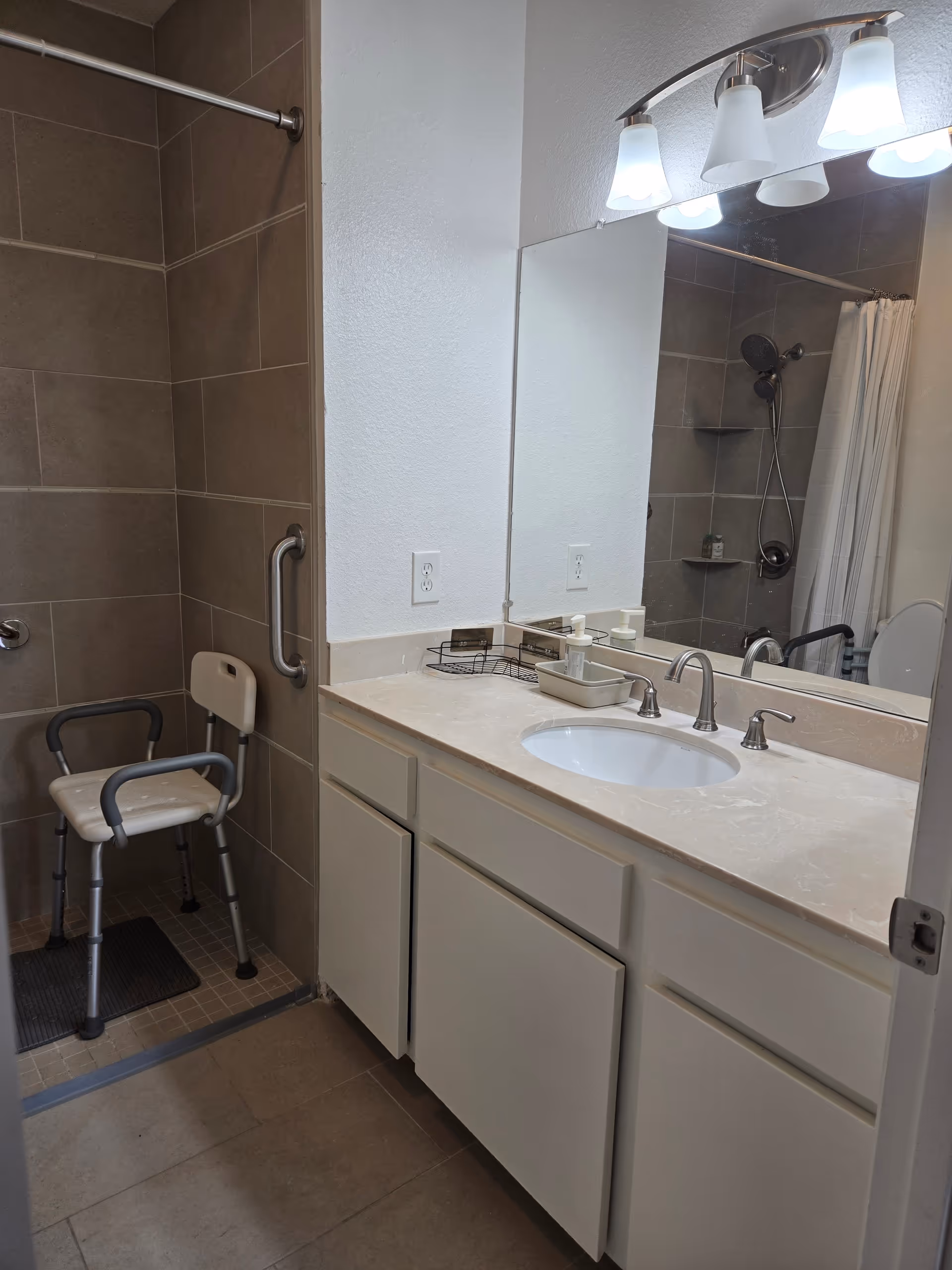 Accessible bathroom with sink, mirror, shower, grab bars, and a shower chair.