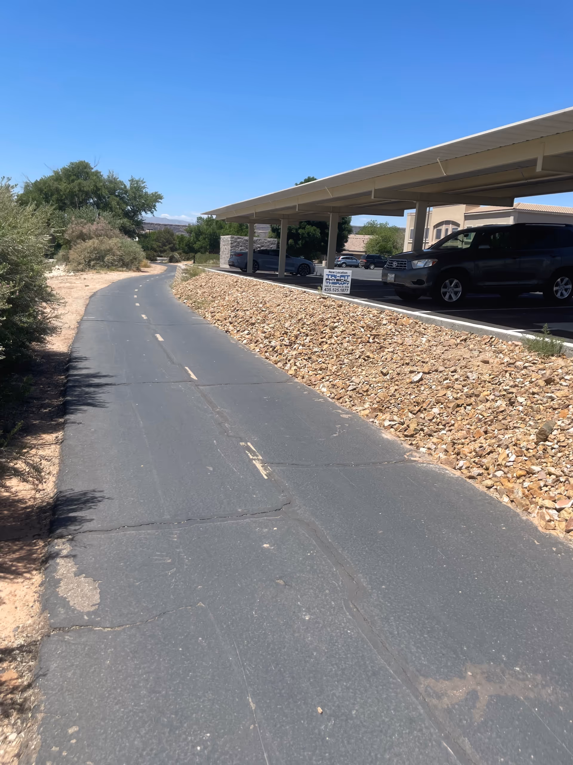 Exterior view of a covered parking area beside a stone retaining wall.