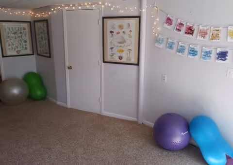 Interior activity room with string lights, framed art, exercise balls, and a closed white door.