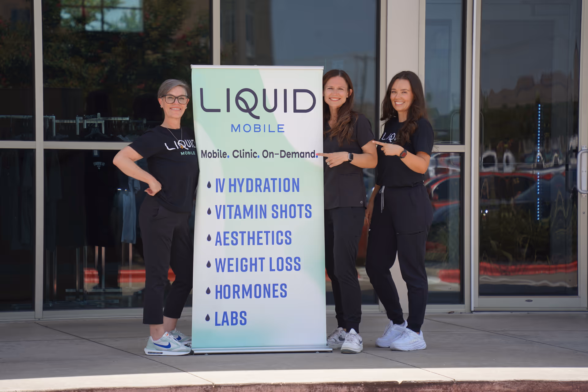 Three staff members pose beside a Liquid Mobile banner outside a clinic entrance.