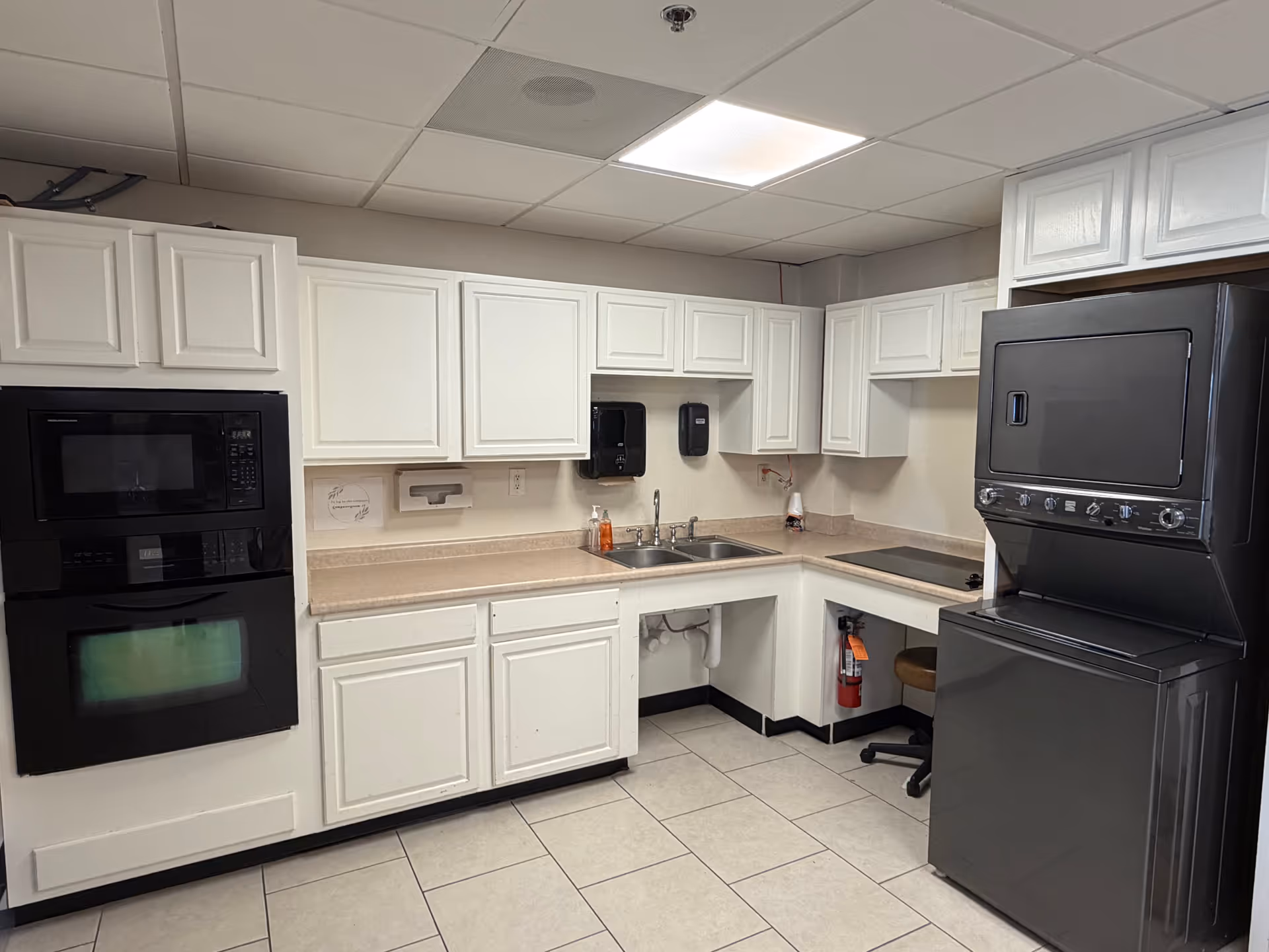 Bright white kitchen with cabinets, sink, and stacked appliances in a senior facility.