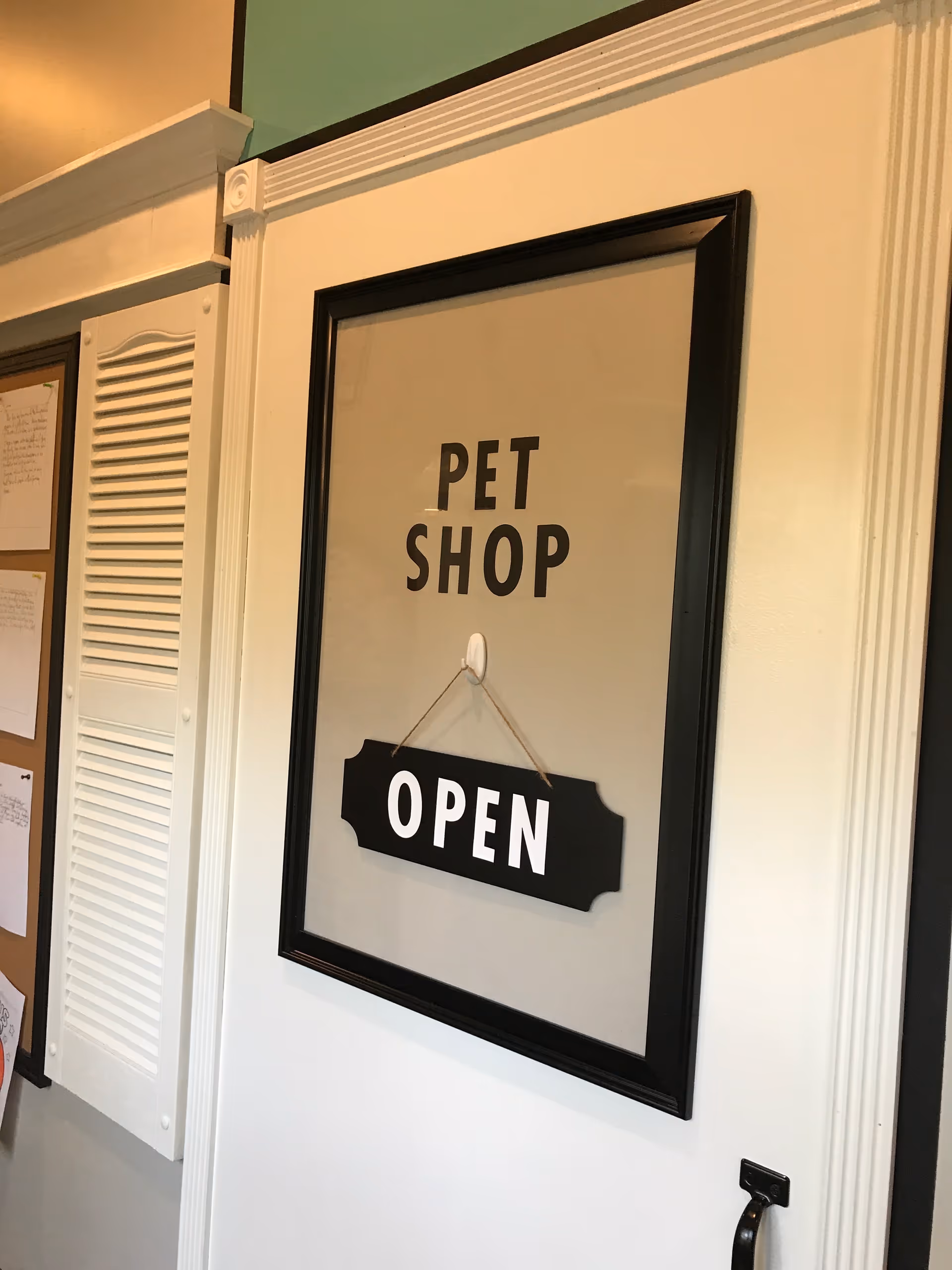 Framed 'PET SHOP OPEN' sign on a white hallway wall.