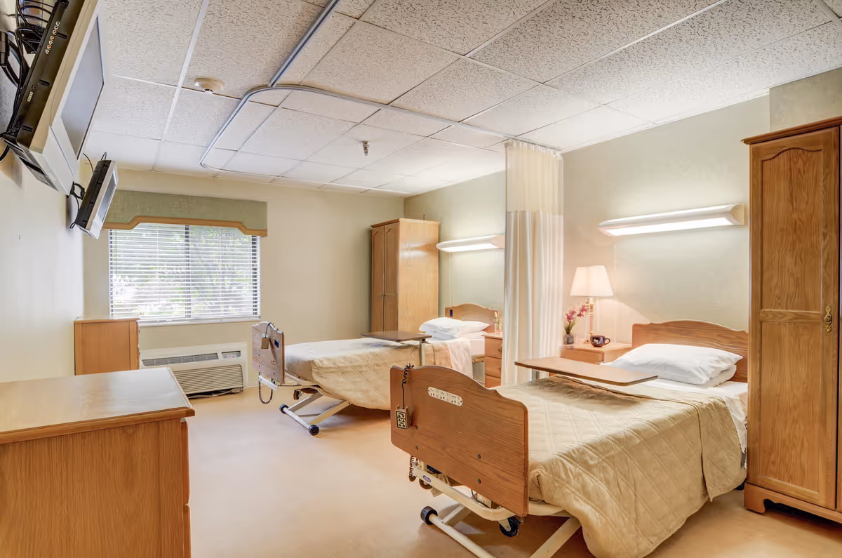 Two hospital beds with wooden headboards in a beige room with a window