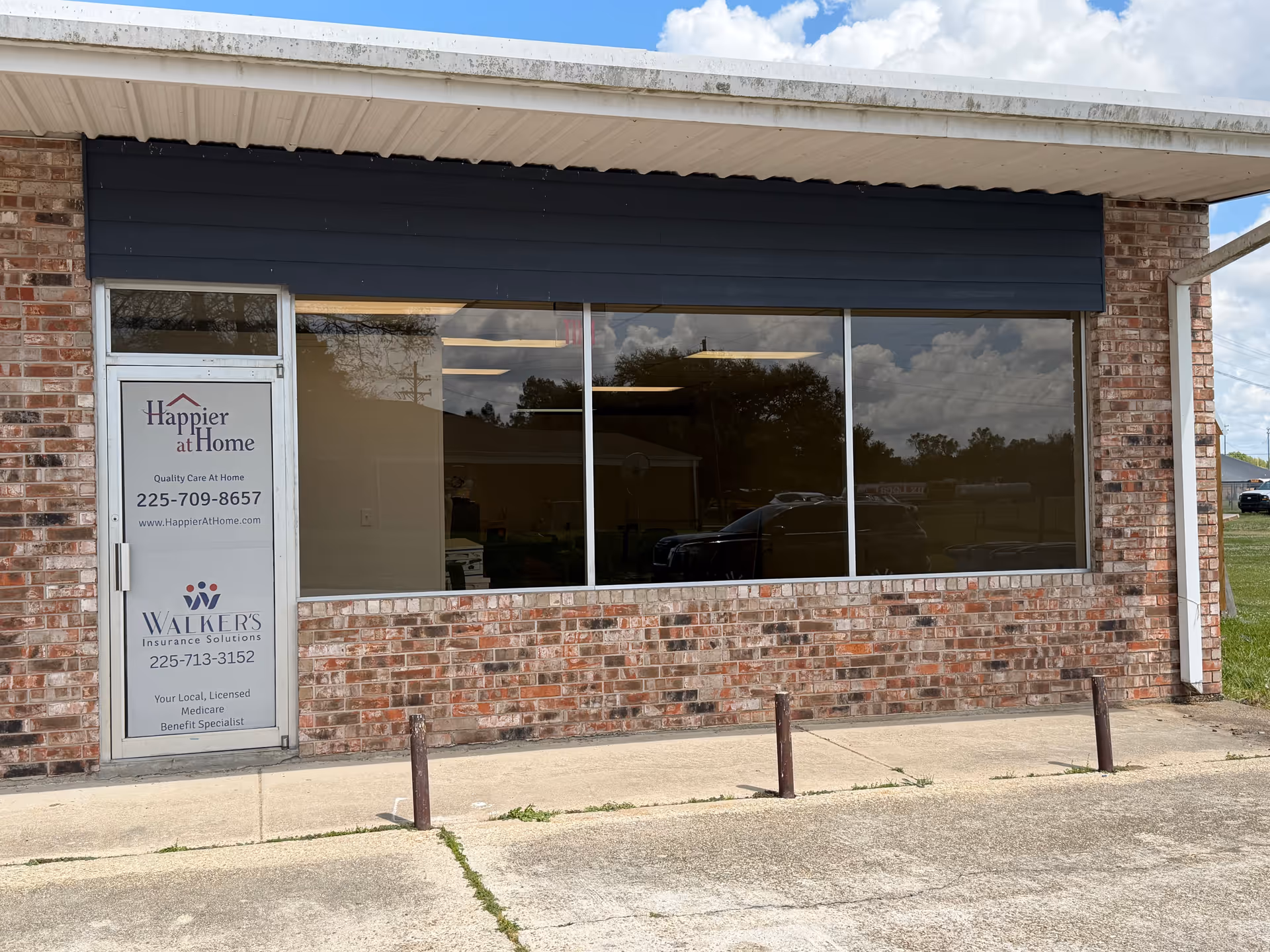 Brick storefront with a large front window and Happier at Home sign on the door.