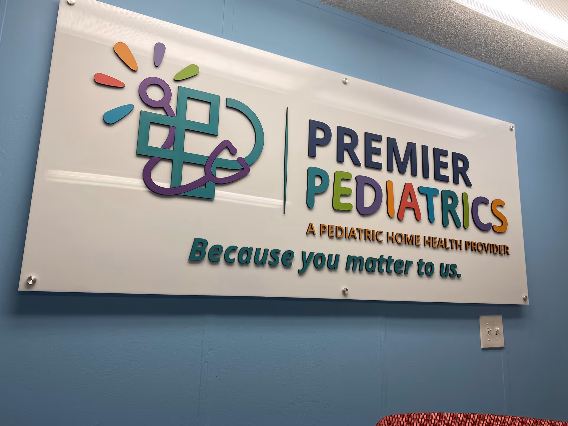 Indoor wall sign for Premier Pediatrics with a colorful logo and slogan.