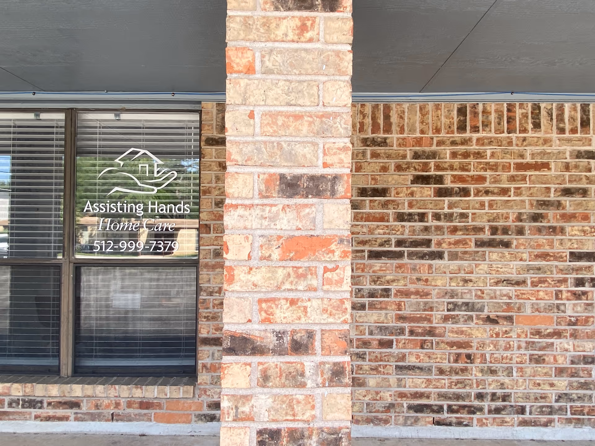 Brick exterior of Assisting Hands Home Care window signage with contact number.
