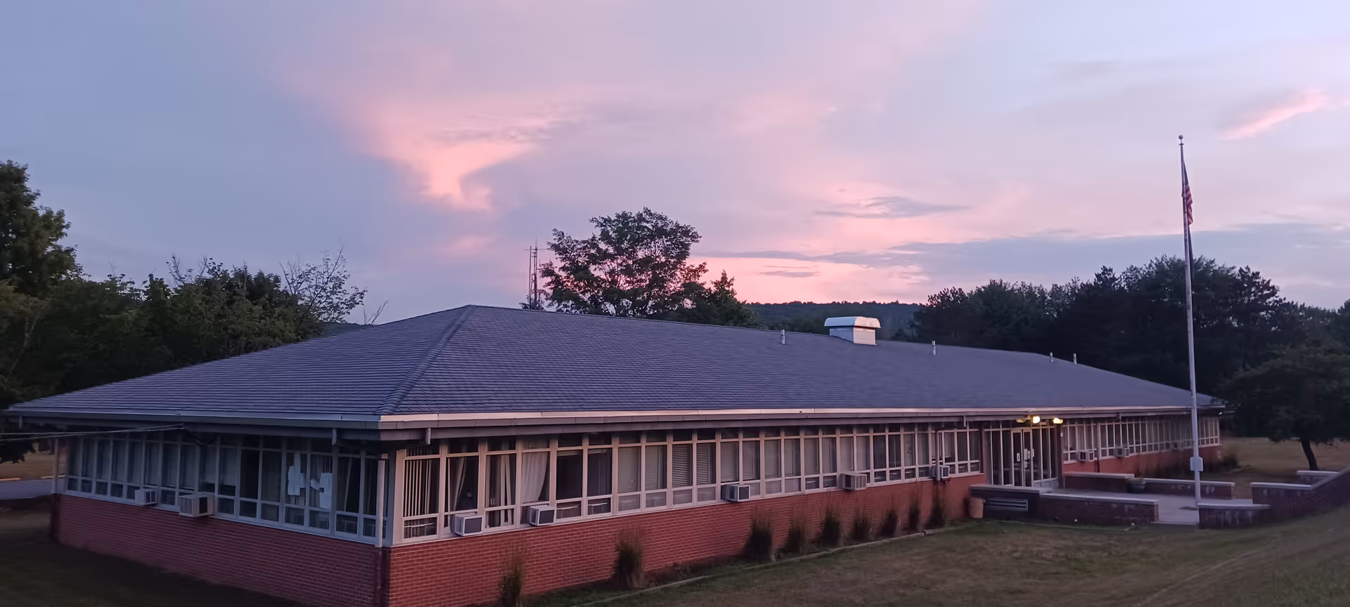 Single-story brick senior living facility with many windows and a flagpole at sunset.