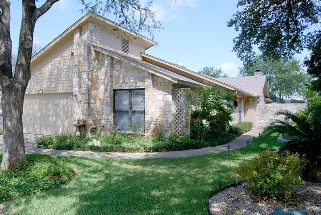 Single-story stone and stucco house with a landscaped front yard, curved walkway, and trees.