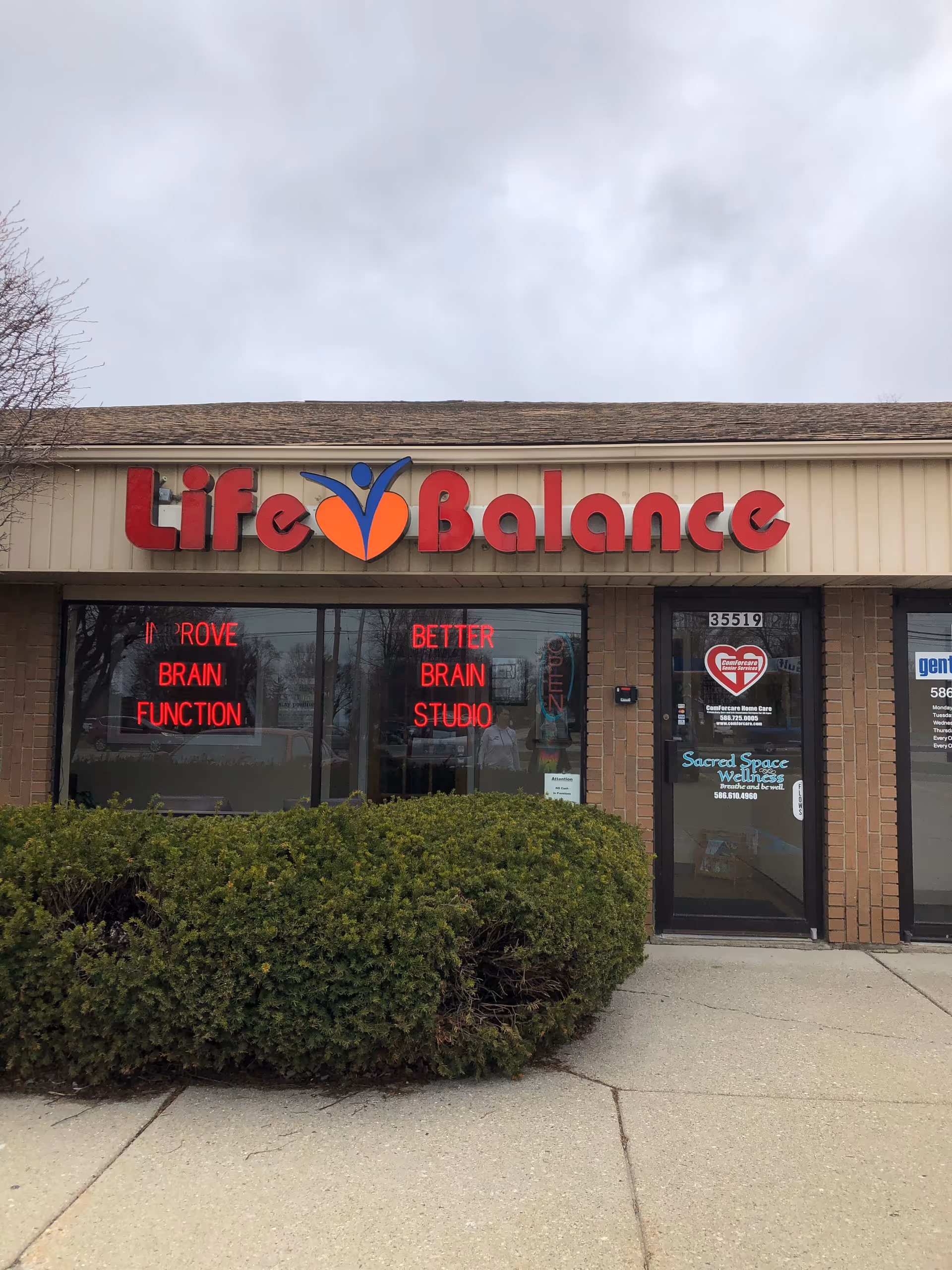Front view of a Life Balance storefront with neon signs and a hedge.