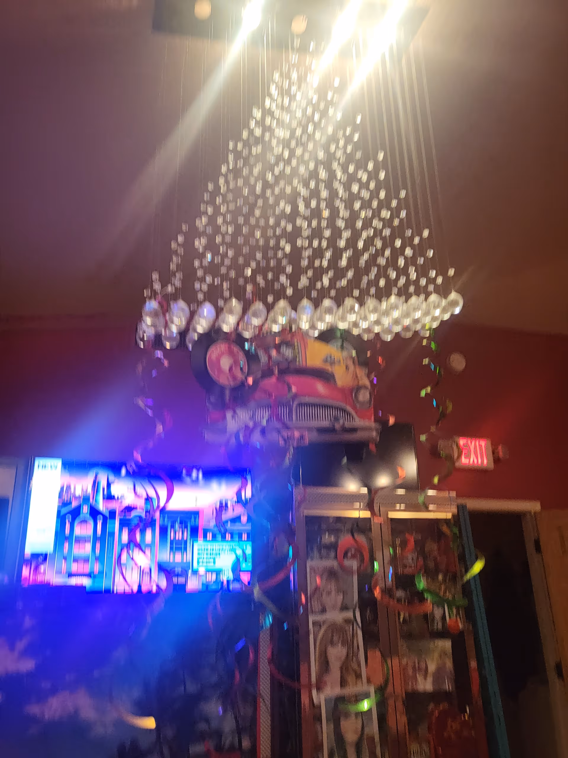 Colorful chandelier-like light fixture hangs above a neon-lit, cluttered facility interior.