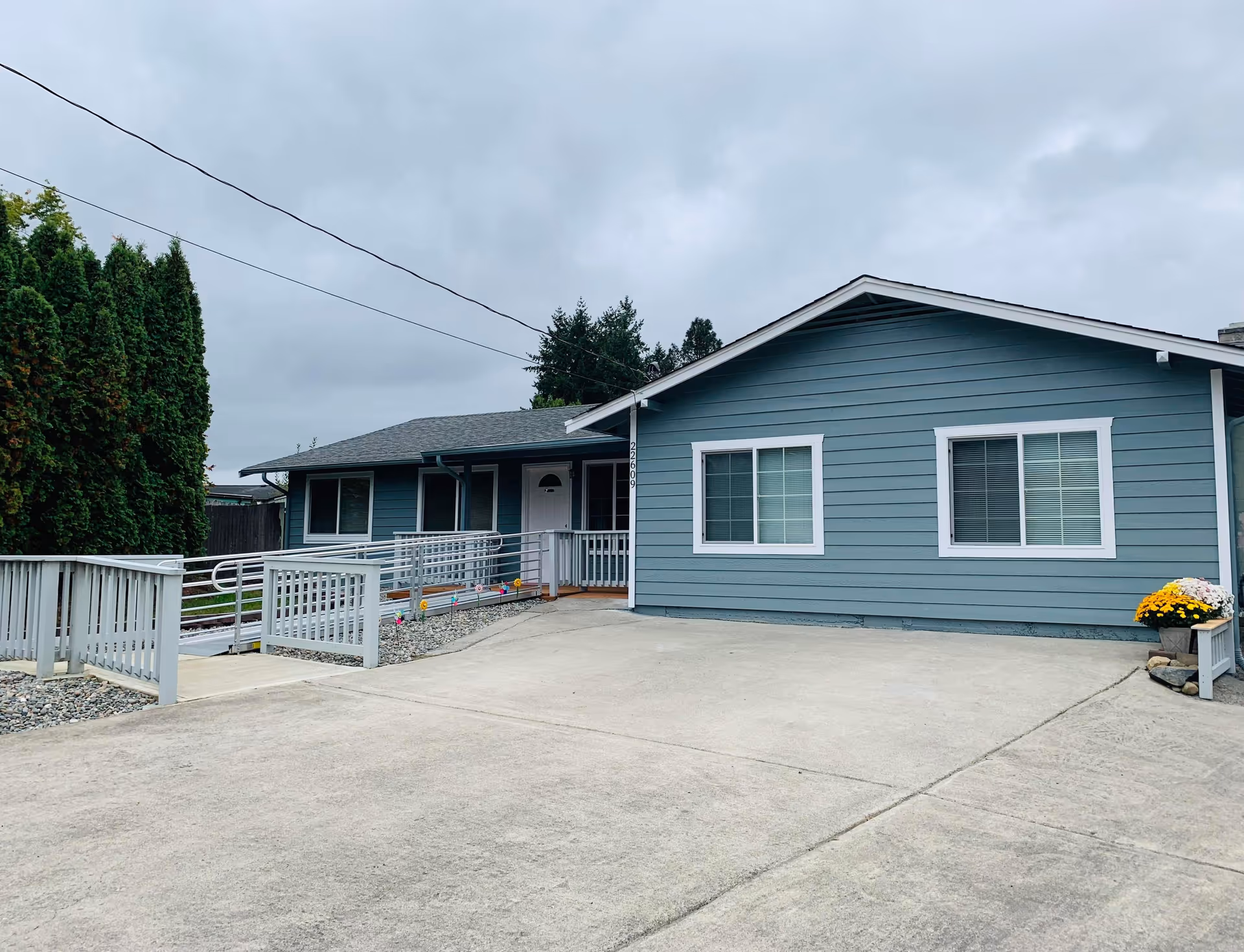 Blue single-story building exterior with ramp leading to front door and potted flowers.