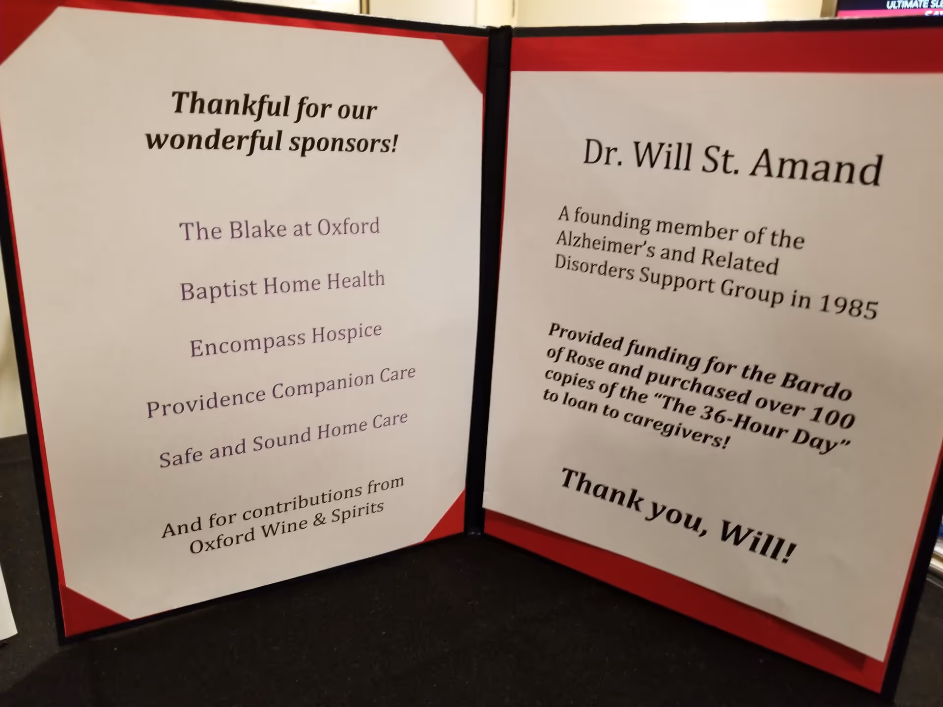 Two-panel display board with sponsor acknowledgments, red accents, on a black table indoors.