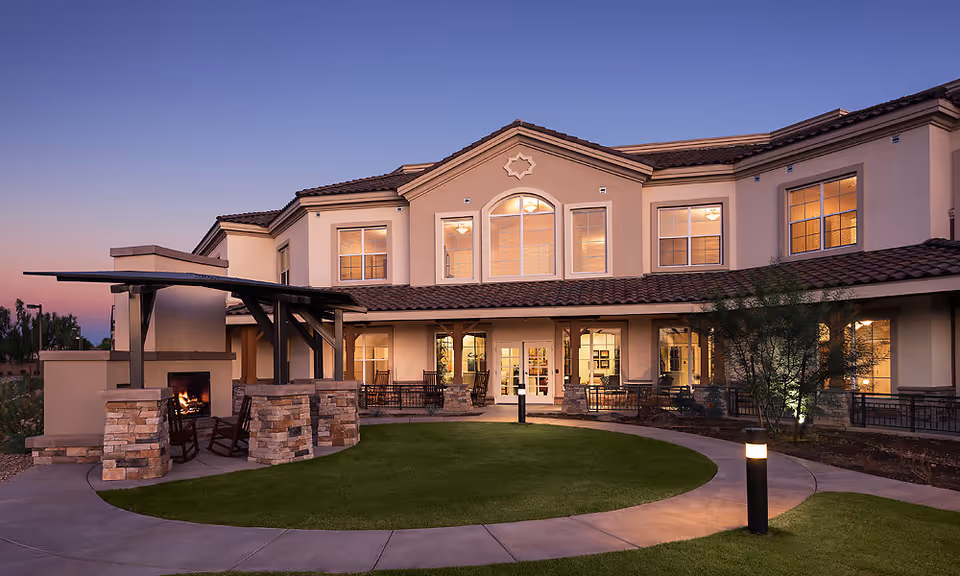 Senior living facility exterior with a lit courtyard and outdoor seating at dusk