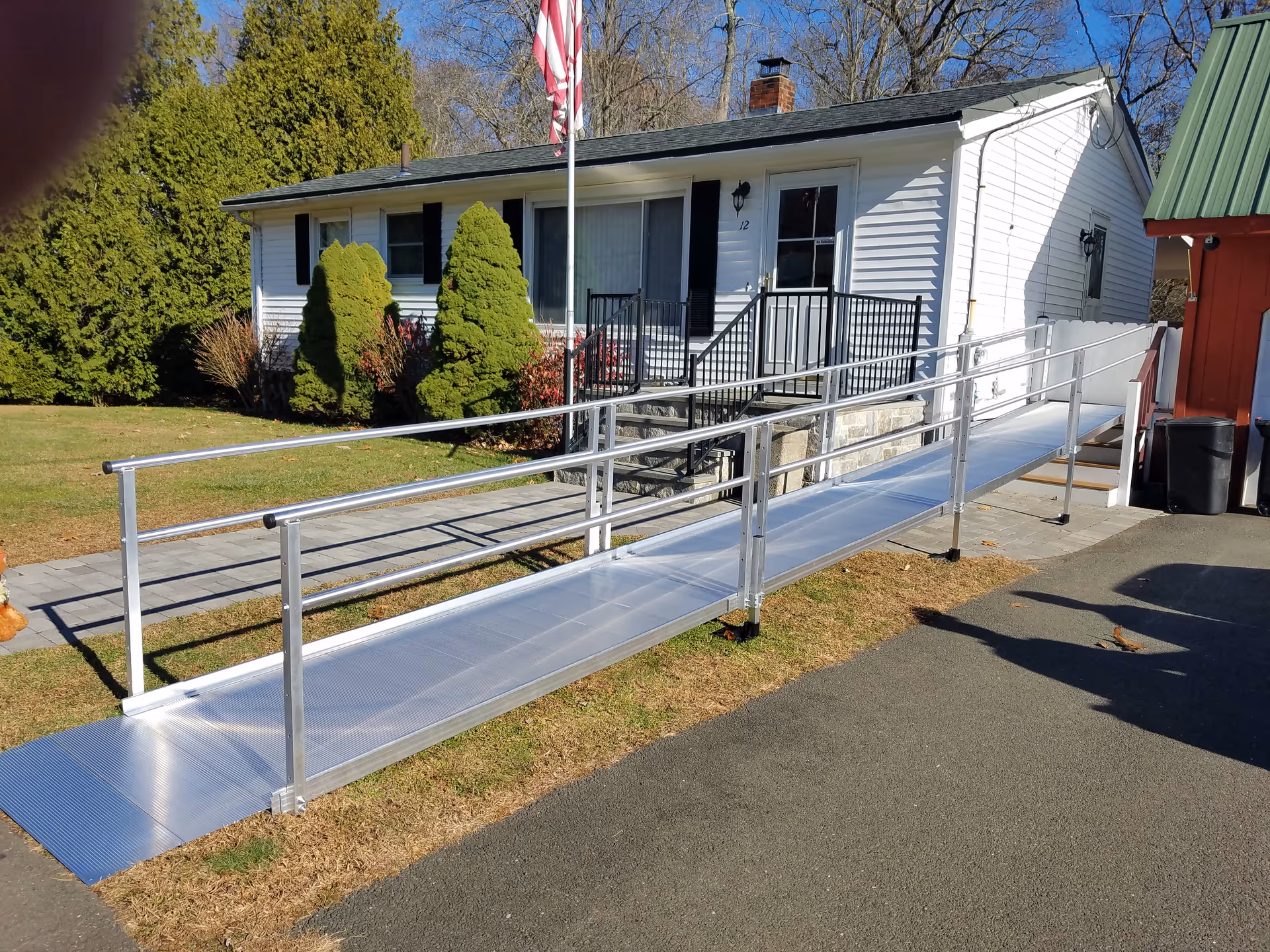 Silver aluminum ramp leads to a white single-story building entrance with flagpole.