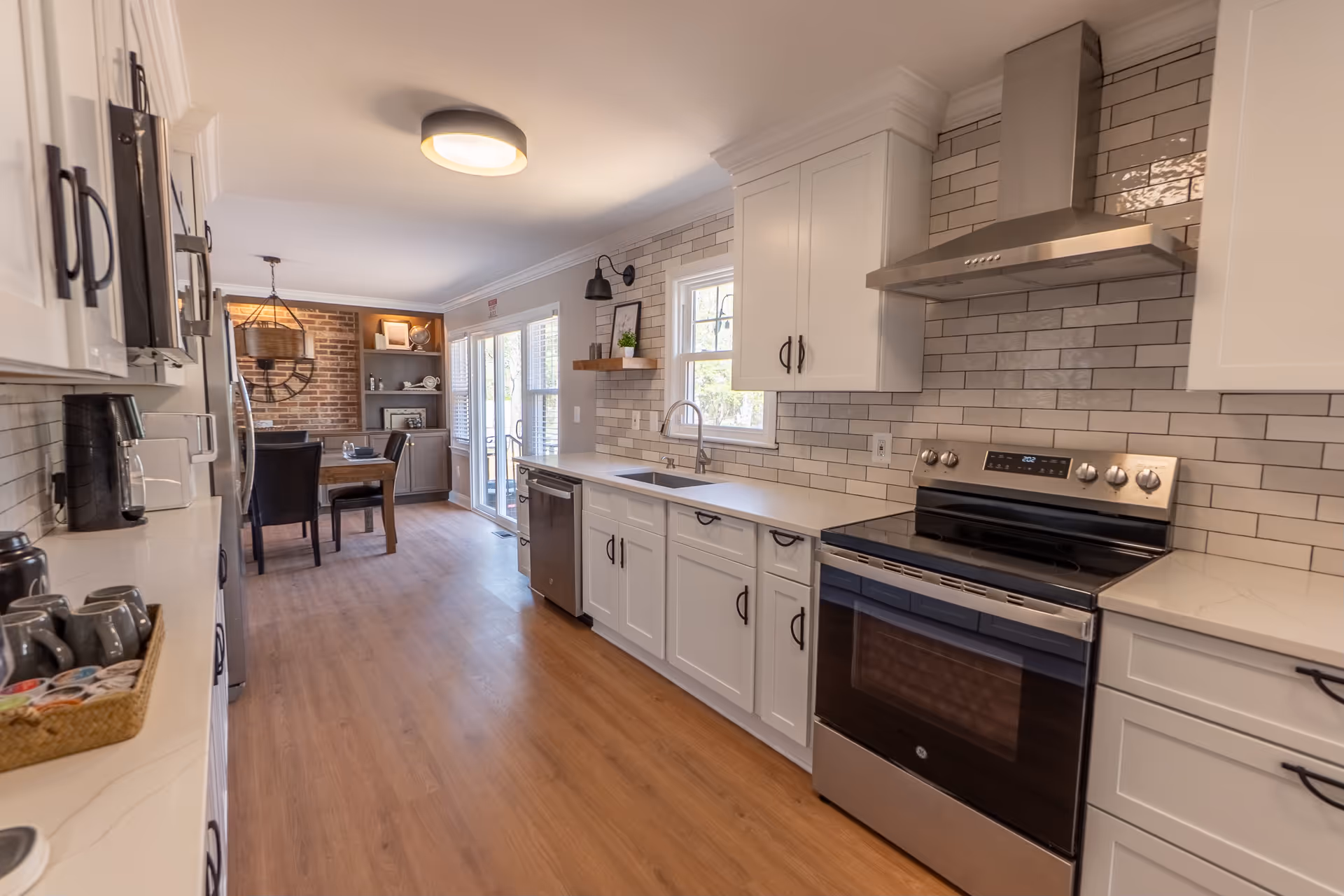 Modern white kitchen with stainless steel appliances, subway tile backsplash, and a dining area in back.
