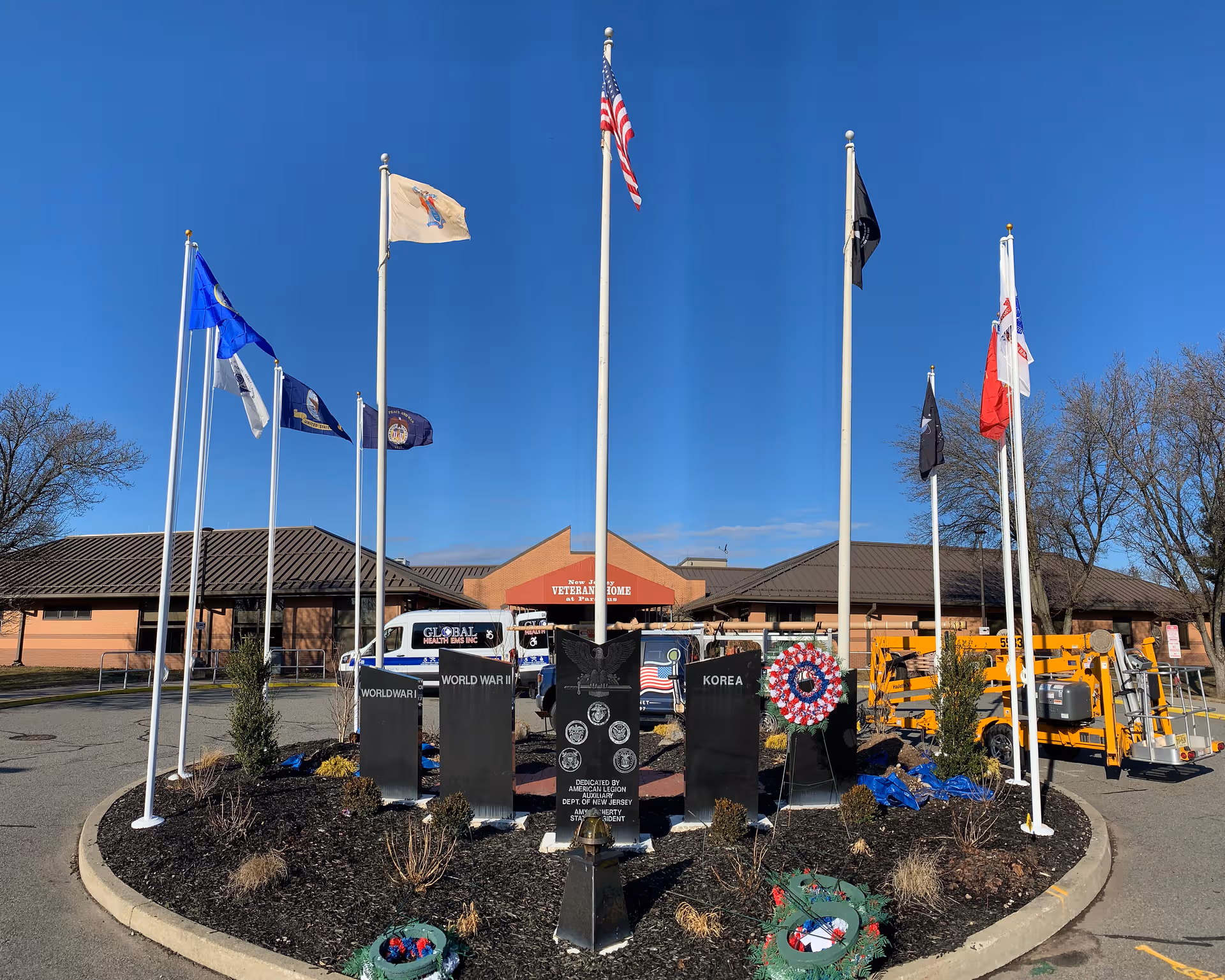 Front of Paramus Veterans Memorial Home with flagpoles, memorial stones, and a clear blue sky.