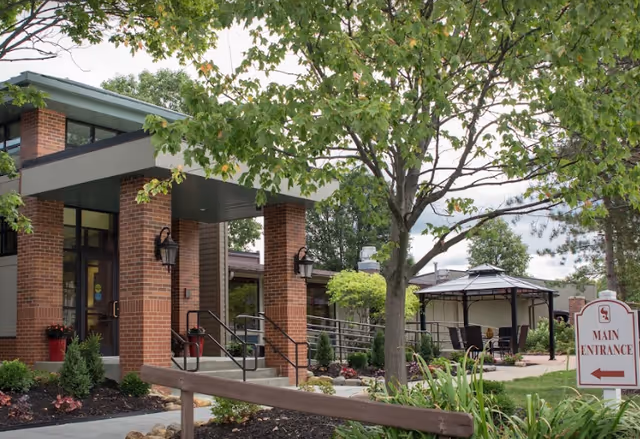 Cardinal Retirement Village exterior with brick entrance, trees, and outdoor seating area.