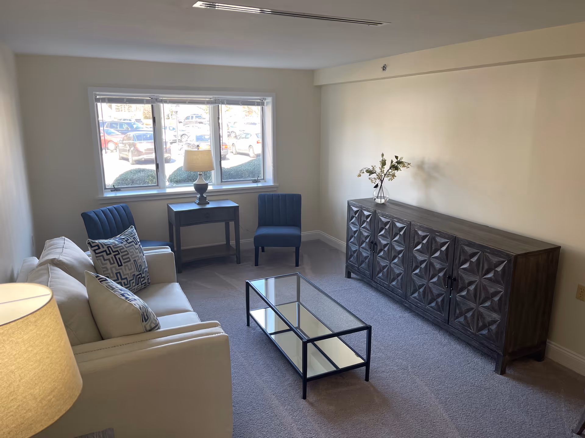 Light-filled living room with sofa, chairs, glass coffee table, and decorative sideboard.