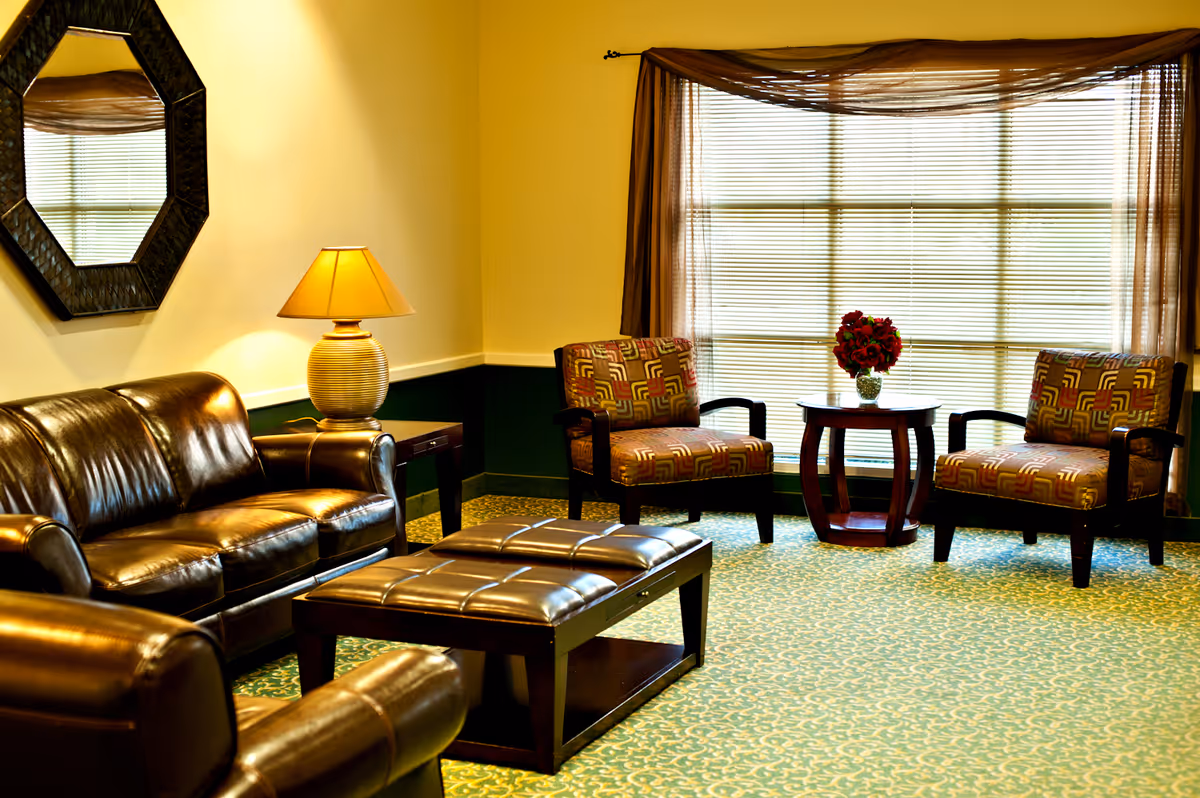 Cozy lounge area with leather seating, armchairs, a coffee table, lamp, and large window blinds.