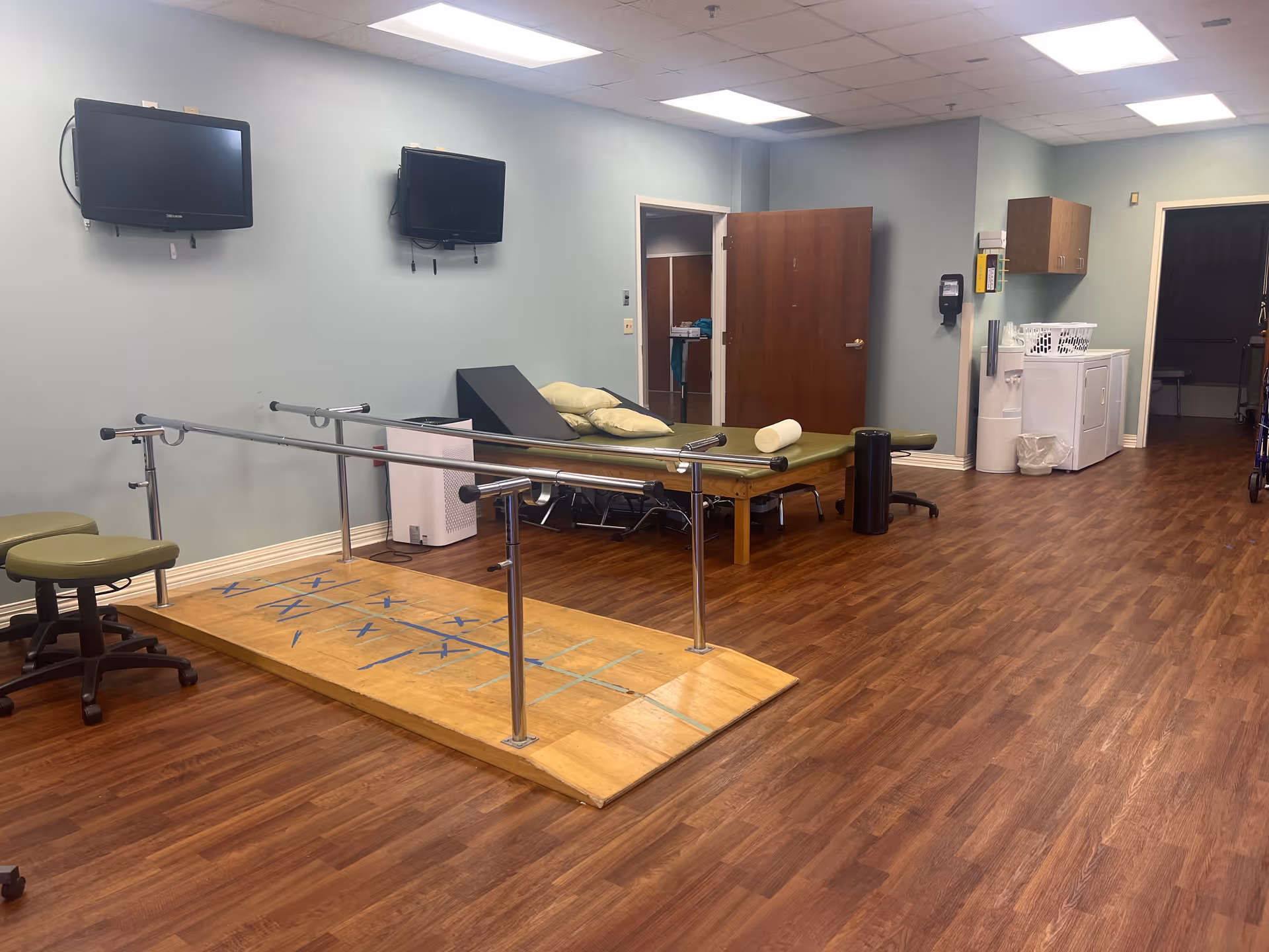 Indoor therapy room with parallel bars and mats in a senior care facility.