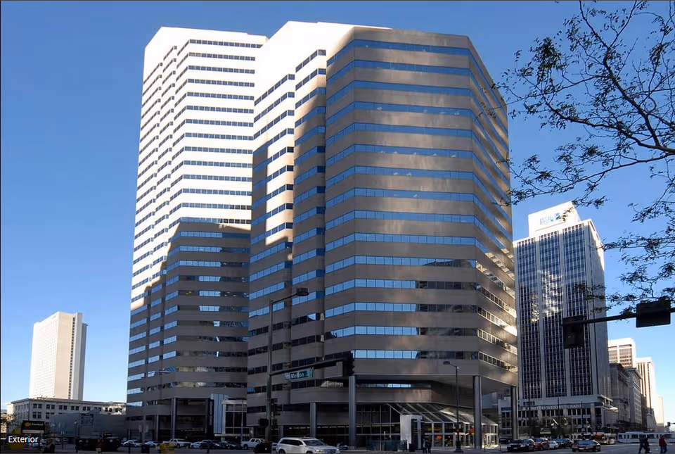 Tall modern office towers along a sunny city street with cars.