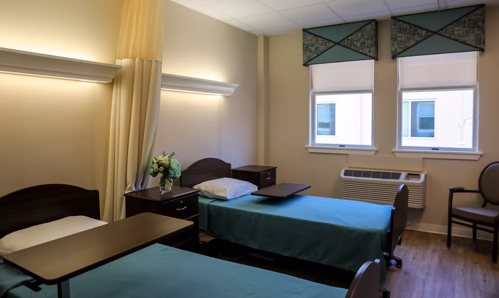 Two single beds with teal bedding in a bright senior living bedroom with nightstands.